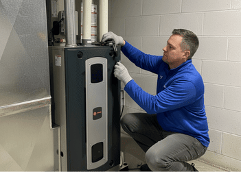 Gloved operator adjusting Trane HVAC gas furnace chassis panel near PVC exhaust piping against concrete block wall.