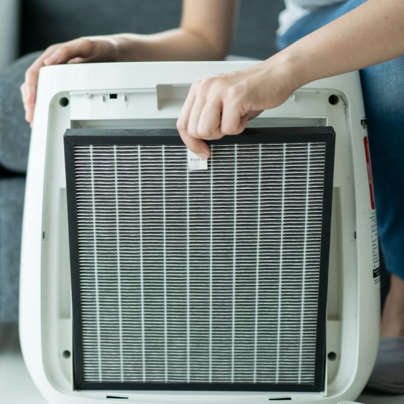 Person replacing the HEPA filter in a modern home air purifier to improve indoor air quality.